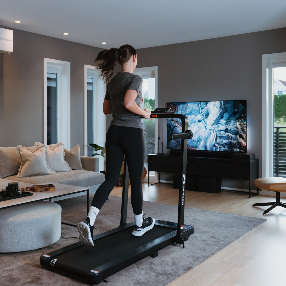 Kvinne som løper på WalkPad foran TV-en