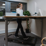 Kvinne som går på WalkPad ved et hevesenkebord